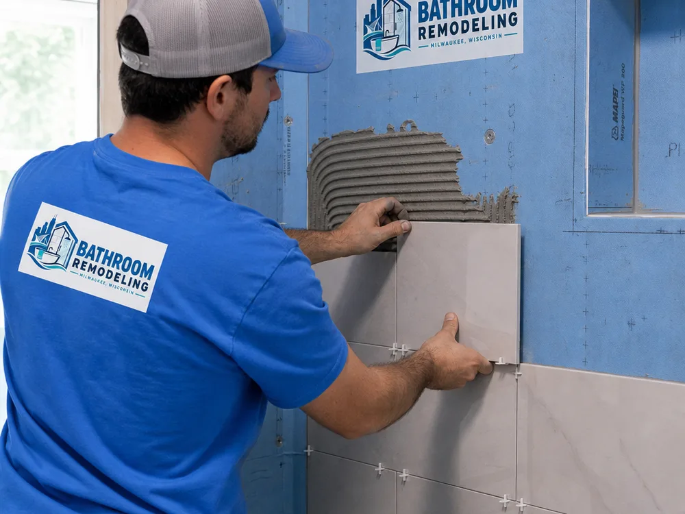 Installer setting tile on a waterproofed shower wall with visible membrane and level lines